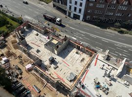 14.08.2025: Auf der Baustelle sind die Arbeiten am Erdgeschoss in unterschiedlichen Bauabschnitten fortgeschritten. Im ersten Bauabschnitt wurde die Bodenplatte bereits vollständig hergestellt, und die Betonarbeiten für die tragenden Wände im Erdgeschoss haben begonnen. Erste Wände und Schächte sind betoniert, die Schalungs- und Bewehrungsarbeiten für weitere Wandabschnitte laufen. Das Arbeitsumfeld ist eingerichtet, Material liegt geordnet bereit, und Gerüste an den Außenkanten sichern die laufenden Arbeiten. Im zweiten Bauabschnitt ist der Rohbau des Erdgeschosses bereits vollständig fertiggestellt. Sämtliche tragenden Wände sind errichtet, und die Baustelle hat nahtlos mit den Rohbauarbeiten im 1. Obergeschoss begonnen. Hier werden aktuell die ersten tragenden Wände des 1. Obergeschosses gestellt, während gleichzeitig vorbereitende Maßnahmen für die das 2.Obergeschoss getroffen werden.