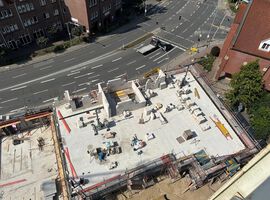 14.08.2025: Auf der Baustelle sind die Arbeiten am Erdgeschoss in unterschiedlichen Bauabschnitten fortgeschritten. Im ersten Bauabschnitt wurde die Bodenplatte bereits vollständig hergestellt, und die Betonarbeiten für die tragenden Wände im Erdgeschoss haben begonnen. Erste Wände und Schächte sind betoniert, die Schalungs- und Bewehrungsarbeiten für weitere Wandabschnitte laufen. Das Arbeitsumfeld ist eingerichtet, Material liegt geordnet bereit, und Gerüste an den Außenkanten sichern die laufenden Arbeiten. Im zweiten Bauabschnitt ist der Rohbau des Erdgeschosses bereits vollständig fertiggestellt. Sämtliche tragenden Wände sind errichtet, und die Baustelle hat nahtlos mit den Rohbauarbeiten im 1. Obergeschoss begonnen. Hier werden aktuell die ersten tragenden Wände des 1. Obergeschosses gestellt, während gleichzeitig vorbereitende Maßnahmen für die das 2.Obergeschoss getroffen werden.