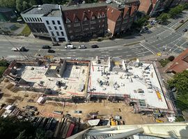 14.08.2025: Auf der Baustelle sind die Arbeiten am Erdgeschoss in unterschiedlichen Bauabschnitten fortgeschritten. Im ersten Bauabschnitt wurde die Bodenplatte bereits vollständig hergestellt, und die Betonarbeiten für die tragenden Wände im Erdgeschoss haben begonnen. Erste Wände und Schächte sind betoniert, die Schalungs- und Bewehrungsarbeiten für weitere Wandabschnitte laufen. Das Arbeitsumfeld ist eingerichtet, Material liegt geordnet bereit, und Gerüste an den Außenkanten sichern die laufenden Arbeiten. Im zweiten Bauabschnitt ist der Rohbau des Erdgeschosses bereits vollständig fertiggestellt. Sämtliche tragenden Wände sind errichtet, und die Baustelle hat nahtlos mit den Rohbauarbeiten im 1. Obergeschoss begonnen. Hier werden aktuell die ersten tragenden Wände des 1. Obergeschosses gestellt, während gleichzeitig vorbereitende Maßnahmen für die das 2.Obergeschoss getroffen werden.